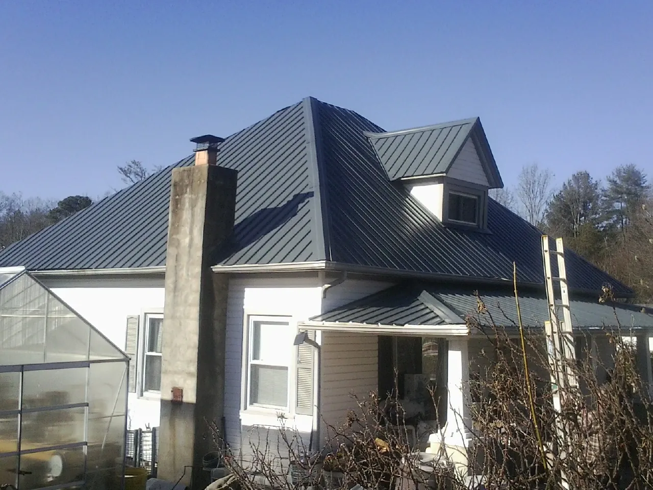 Dark blue standing seam metal roof on a white farmhouse with dormer — Slate & Tile Roof Repair by Roofing Brothers in Mcpherson