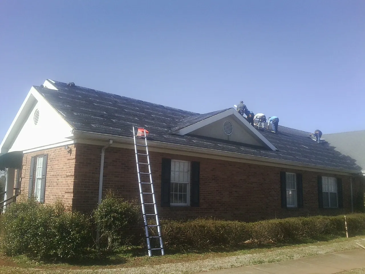 Crew tearing shingles off a brick ranch roof with a ladder set — Emergency Roof Repair work by our crew in Mcpherson