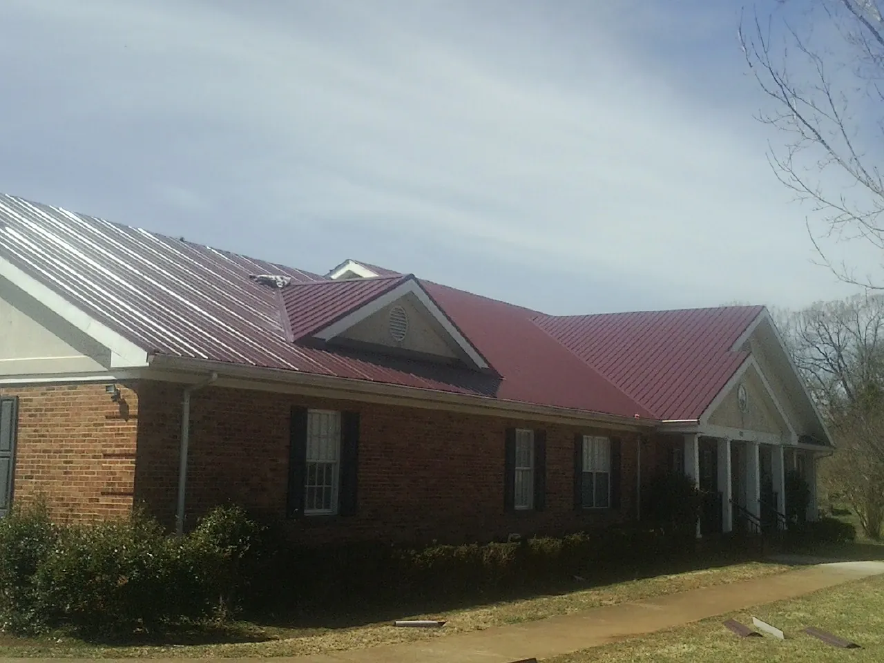 Red metal roof with gabled entries on a long brick building, from a Hail Damage Roof Repair job in Mcpherson