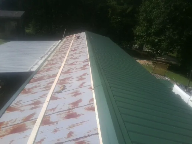 Old rusted panels beside newly installed green metal roofing — Wind Damage Roof Repair by Roofing Brothers in Mcpherson