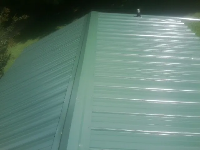 New green metal panels meeting at the ridge of a roof — Flat Roof Repair work by our crew in Mcpherson