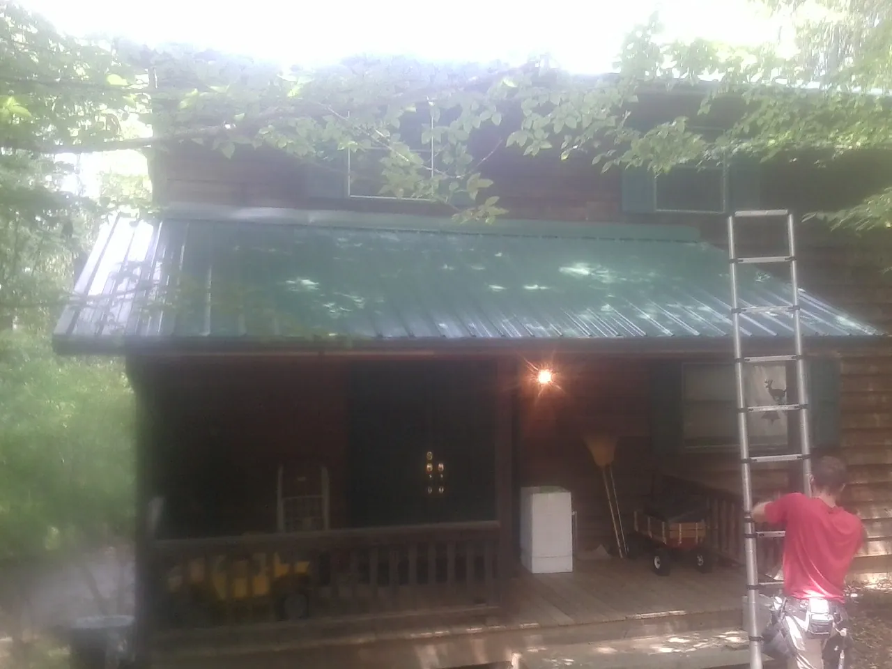 Worker on a ladder at the green porch roof of a wooded cabin in Mcpherson