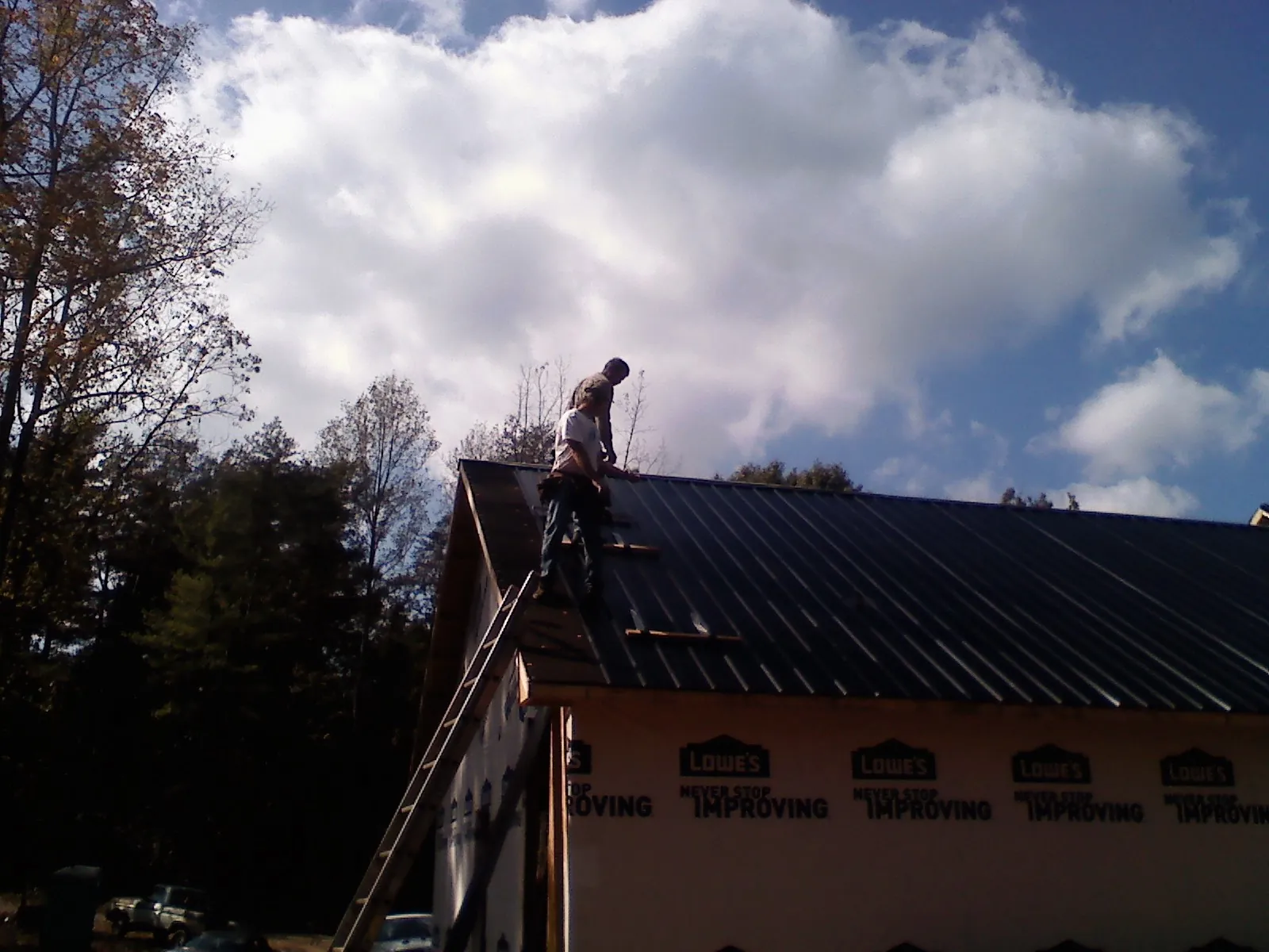 Roofer fastening dark metal panels high against a cloudy sky, from a Roof Inspection job in Mcpherson