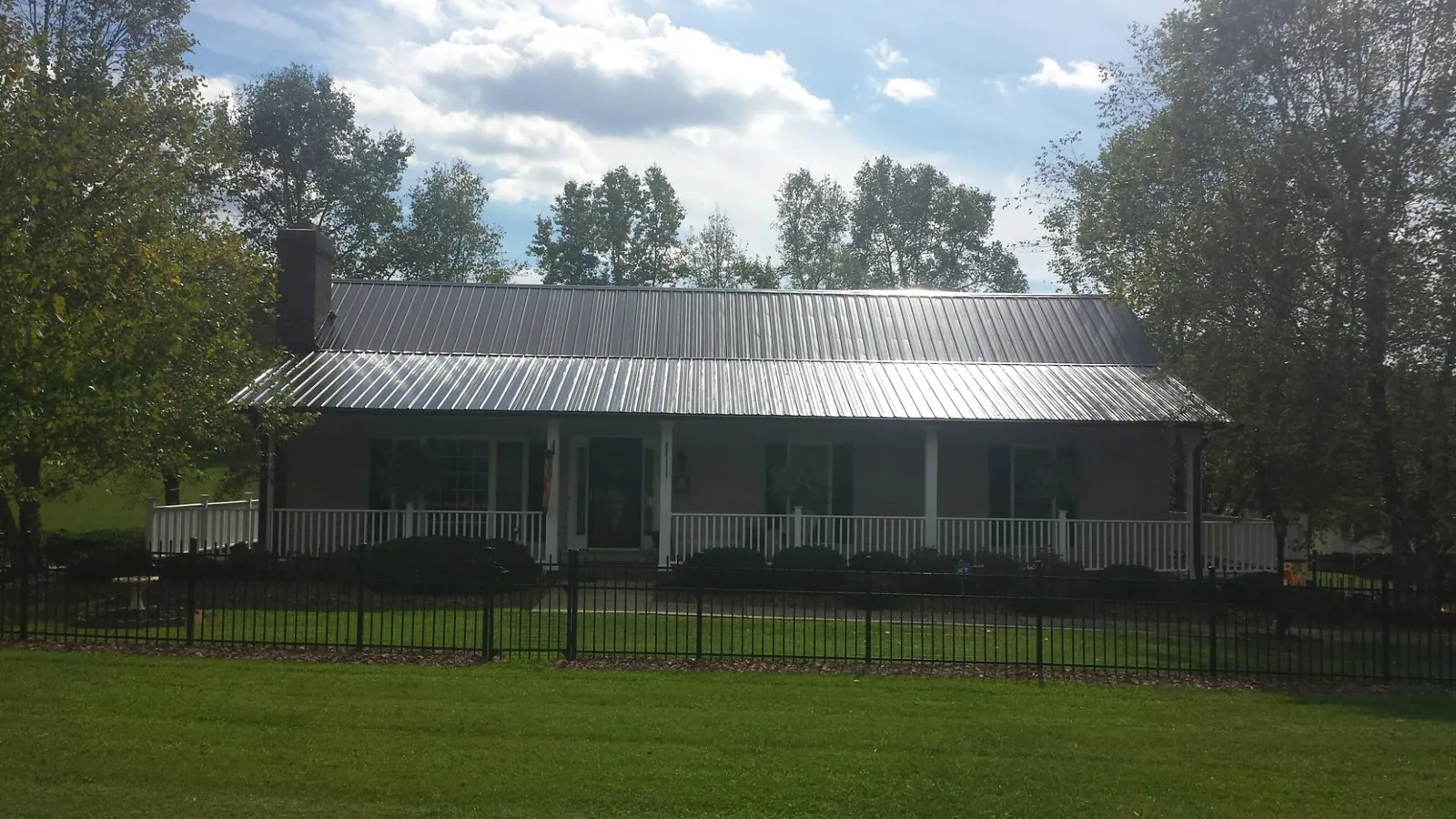 Gray metal roof on a brick ranch with a full width front porch — Gutter Guard Installation work by our crew in Mcpherson