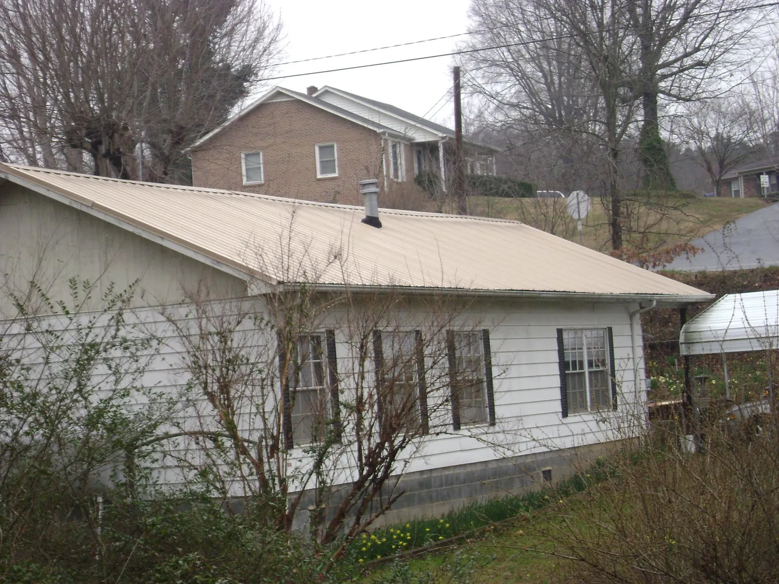 Tan metal roof on a white sided house set into a hillside — Commercial Roofing by Roofing Brothers in Mcpherson
