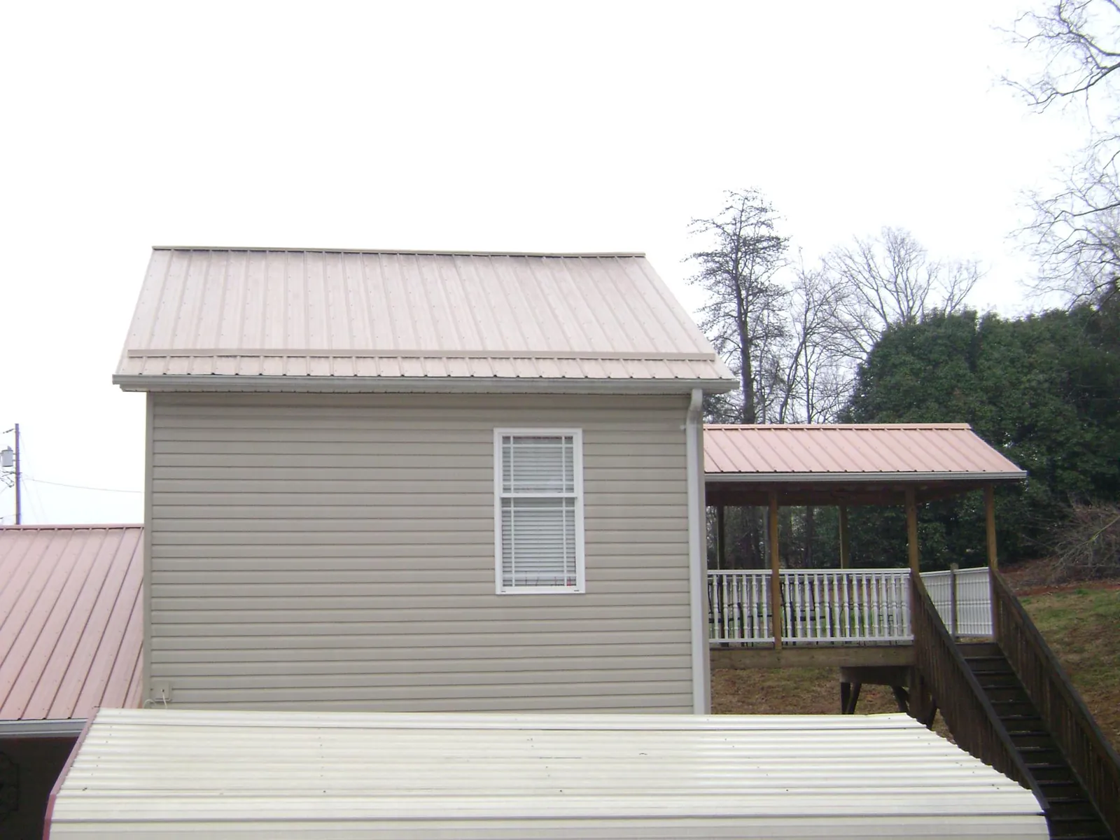 Tan metal roofs on a two story addition and attached porch, from a Roof Replacement job in Mcpherson