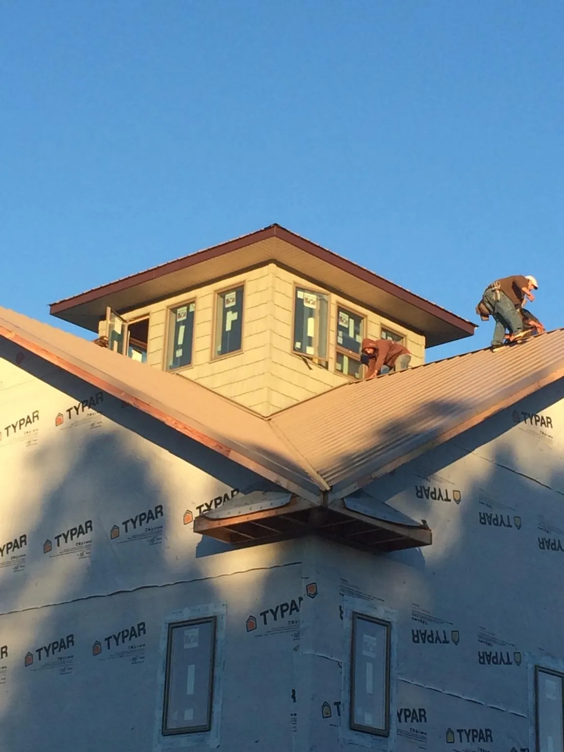 Roofers working around a rooftop cupola on a new metal roof at sunset — Roof Waterproofing in Mcpherson by Roofing Brothers